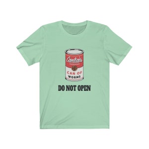 Puede incluir: Una camiseta verde claro con un gr&aacute;fico de una lata roja etiquetada "Caecilian's Condensed Can of Worms" con el texto "Do Not Open" en negro.