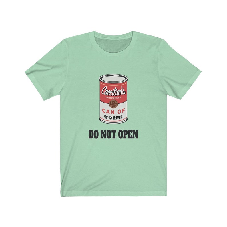 Puede incluir: Una camiseta verde claro con un gr&aacute;fico de una lata roja etiquetada "Caecilian's Condensed Can of Worms" con el texto "Do Not Open" en negro.