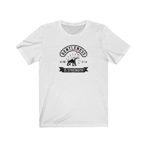 Puede incluir: Camiseta blanca con un gr&aacute;fico negro que presenta un elefante y las palabras "GENTLENESS IS STRENGTH". El dise&ntilde;o incluye los a&ntilde;os "20" y "21" con acentos de estrella. La camiseta est&aacute; hecha de un material suave y c&oacute;modo.