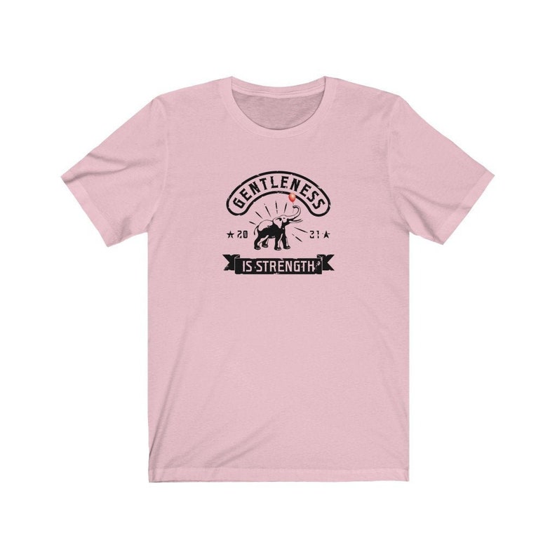 Puede incluir: Camiseta rosa claro con un gr&aacute;fico negro que representa un elefante y el texto &laquo;GENTLENESS IS STRENGTH&raquo;. El dise&ntilde;o incluye los a&ntilde;os &laquo;20&raquo; y &laquo;21&raquo; con detalles de estrellas. La camiseta es de material suave.