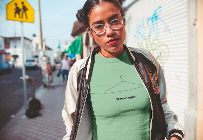 May include: A green t-shirt with a black outline of a hanger and the text "Never again."