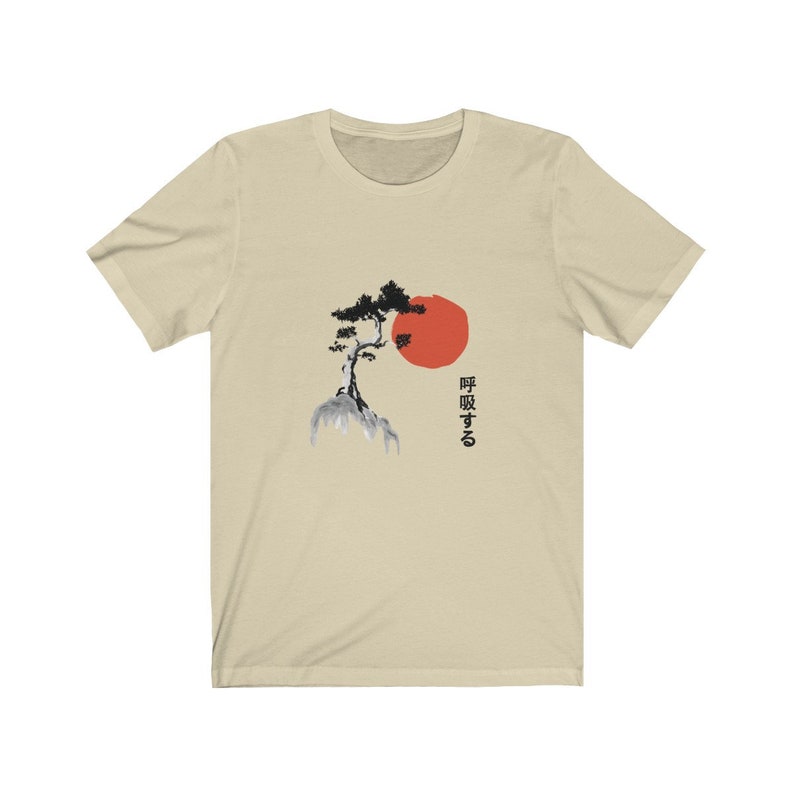 Puede incluir: Una camiseta beige con una ilustraci&oacute;n en blanco y negro de un &aacute;rbol en una roca con un sol rojo detr&aacute;s. El texto japon&eacute;s "呼吸する" est&aacute; impreso en el lado derecho de la camiseta.