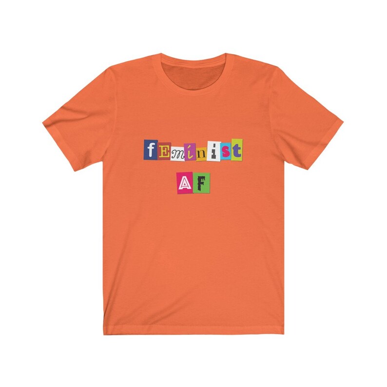 May include: Orange short-sleeved t-shirt with the text "feminist AF" in colorful letters.