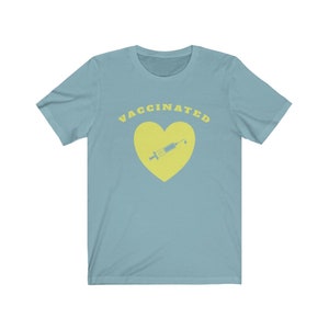May include: A light blue t-shirt with the text "VACCINATED" in yellow letters. A yellow heart with a yellow syringe inside is below the text.