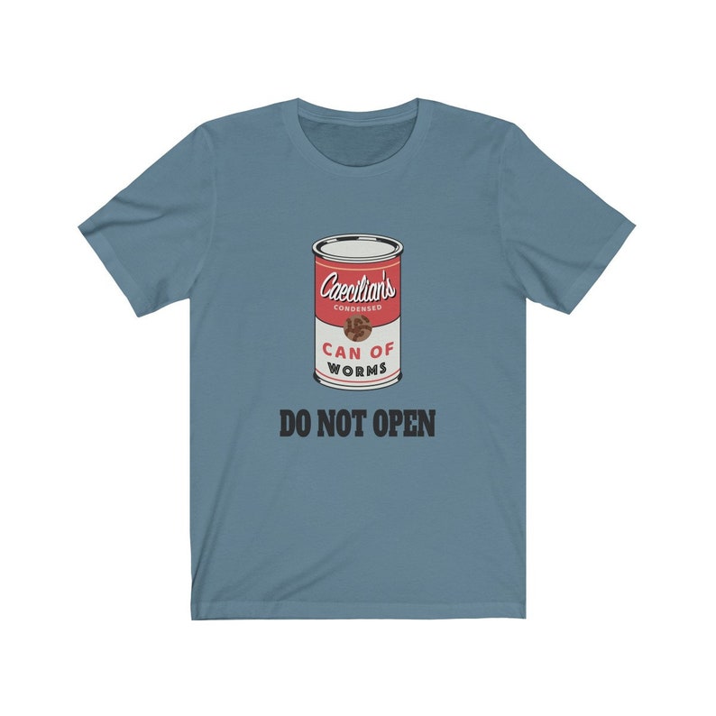Puede incluir: Una camiseta azul con un gr&aacute;fico de una lata roja etiquetada "Caecilian's Condensed Can of Worms" con el texto "Do Not Open" debajo.