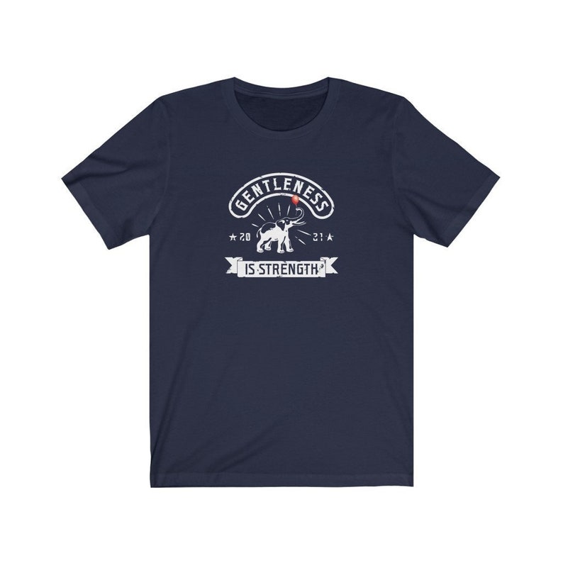 Puede incluir: Camiseta azul marino con un gr&aacute;fico blanco. El gr&aacute;fico presenta las palabras "GENTLENESS IS STRENGTH" con una ilustraci&oacute;n de elefante. El dise&ntilde;o incluye los a&ntilde;os "20" y "21" con acentos de estrella.