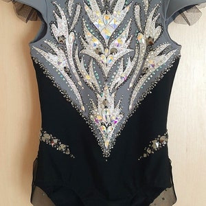 May include: A black and grey leotard with a high neckline and short sleeves. The leotard is decorated with rhinestones and a geometric design.