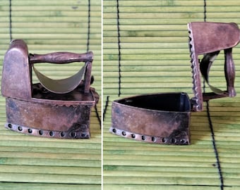 May include: A vintage-style iron pencil sharpener with a hinged lid. The sharpener is made of metal and has a brown finish. The lid is open, revealing the sharpening mechanism.