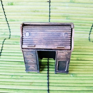 May include: A vintage-style wooden pencil sharpener shaped like a roll-top desk. The desk has three drawers on the left side and a door on the right side. The desk is brown and has a black base.