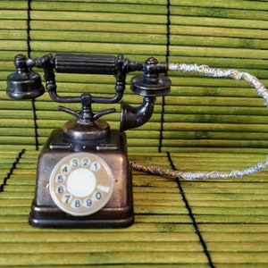 May include: A vintage-style rotary phone pencil sharpener with a silver cord and a black and brown finish. The phone has a dial with the numbers 1 through 0.