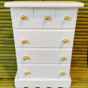 May include: White wooden dresser with four drawers and gold knobs. The dresser has a distressed finish.