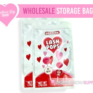 May include: Two clear plastic bags with a Valentine's Day theme. Each bag contains two pink and red lollipops with the text "Lash Pops" and "Charms" on the front. The lollipops have the text "Be Mine" and "Hug Me" on them. The bags have a net weight of 1.2 oz (226 g).