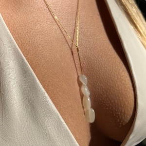 Op de afbeelding: Een gouden ketting met een hanger gemaakt van vier witte stenen. De stenen zijn gevormd als kleine, platte kiezelsteentjes.