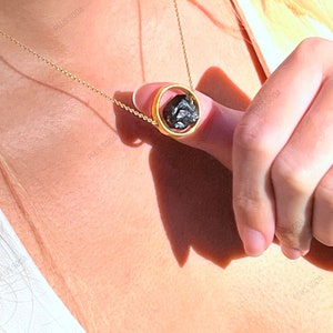 Pode incluir: Um colar de corrente de ouro com um pingente que apresenta uma pedra preta envolta em um círculo dourado.