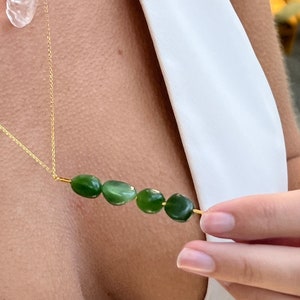 Può includere: Una collana con catena dorata con un ciondolo di cristallo trasparente e una fila di cinque pietre di giada verde.