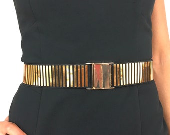 May include: A gold-toned belt with a black leather backing and a rectangular buckle. The belt has a series of vertical gold bars.