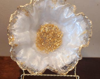 Puede incluir: Plato en forma de flor de resina blanca con detalles de pan de oro sobre un soporte de metal dorado.