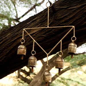 May include: A gold metal wind chime with six bells hanging from a triangular frame. The bells are made of a brass-like metal and have a slightly aged patina.