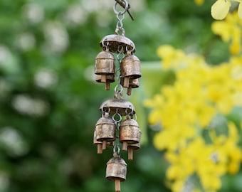 May include: A set of small, silver bells hanging from a chain. The bells are arranged in a tiered fashion, with the largest bell at the top and the smallest bell at the bottom. The bells are hanging from a branch, and the background is blurred.