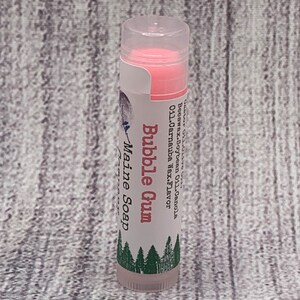 May include: A pink lip balm tube with a white label that reads "Bubble Gum" and "Maine Soap". The label also lists the ingredients: "Olive Oil, Canola, Beeswax, Soy Bean Oil, Carnauba Wax, Flavor"