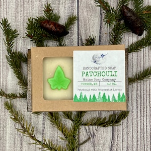 May include: A bar of handmade soap in a cardboard box with a green leaf design. The soap is labeled "HANDCRAFTED SOAP PATCHOULI Maine Soap Company TURNER, ME 4.5 OZ. Patchouli with Peppermint Leaves".