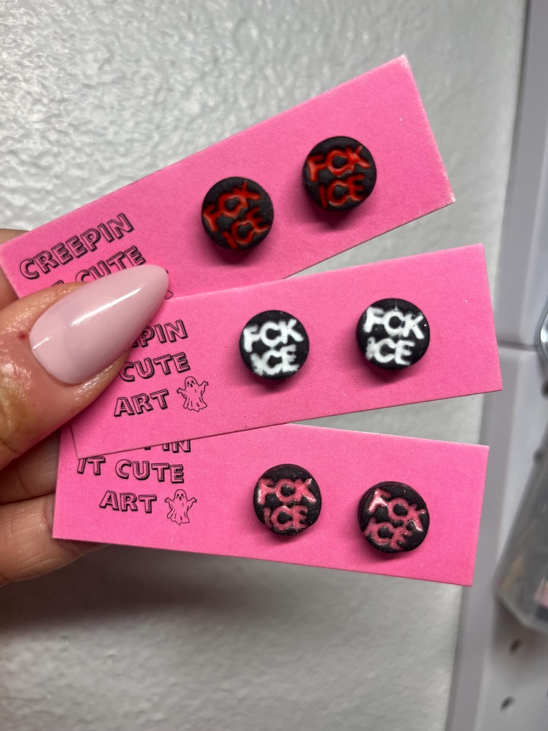 May include: Three pairs of round stud earrings displayed on pink cards. The earrings have black and red, black and white, and black and pink designs with the text "FCK ICE" or a similar design. The cards are printed with the text "CREEPIN CUTE ART".