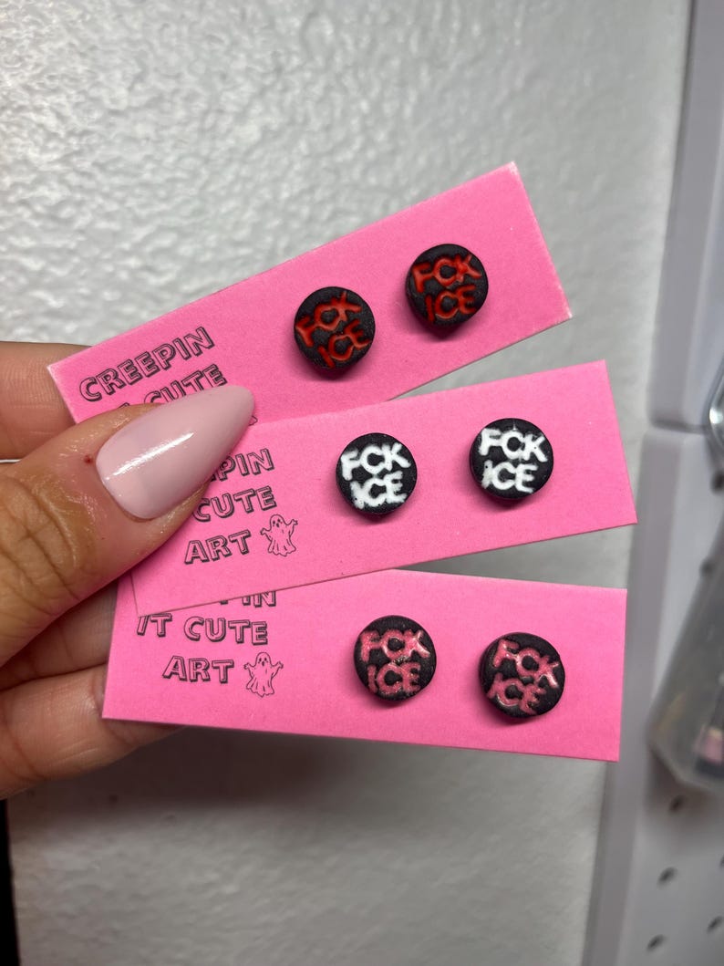 May include: Three pairs of round stud earrings on pink cards. The earrings have black backgrounds with the words "FCK ICE" in white or red. The cards have the text "CREEPIN CUTE ART".