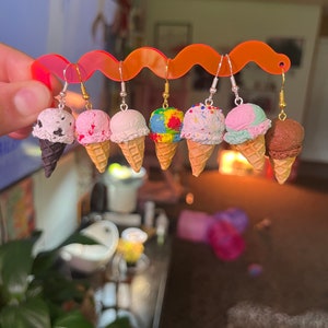 May include: A set of eight ice cream cone earrings. The earrings are made of polymer clay and feature different ice cream flavours, including chocolate, strawberry, vanilla, and rainbow sprinkles. The earrings are attached to silver hooks.