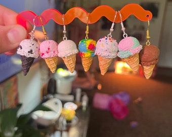 May include: A set of eight ice cream cone earrings. The earrings are made of polymer clay and feature different ice cream flavors, including chocolate, strawberry, vanilla, and rainbow sprinkles. The earrings are attached to silver hooks.