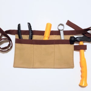 May include: A brown canvas tool belt with four pockets. The belt has a brown strap and is filled with tools, including a hammer, pliers, a screwdriver, and a wrench.