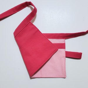 Pale pink cotton toolbelt for small children, with three large pockets and dark pink trim and ties. There is an added loop off to one side for hanging a small tool. This view shows the back, which is dark pink to match the trim.