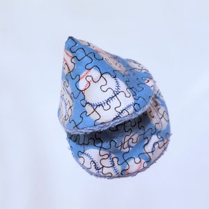 May include: A blue fabric cone with a white and black jigsaw puzzle pattern and red stitching. The fabric has a white fringe around the edge.