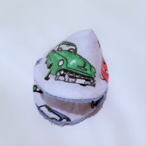 May include: A white fabric cone-shaped burp cloth with a blue trim. The fabric has a pattern of vintage cars in green, red, and blue.