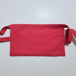 Pale pink cotton toolbelt for small children, with three large pockets and dark pink trim and ties. There is an added loop off to one side for hanging a small tool. This view shows the back, which is dark pink to match the trim.