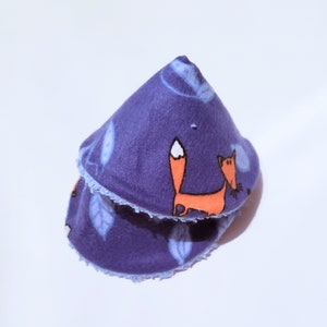 May include: A purple fleece cone-shaped pet bed with a blue trim and a fox print. The fox is orange with a white tail tip and is walking to the right.