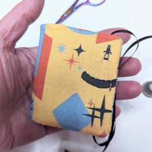 May include: A small yellow fabric pouch with a blue, red, and black geometric pattern. The pouch has a black ribbon attached to it.