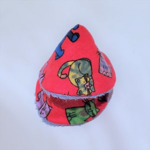 May include: A red fabric cone-shaped cat toy with a blue and white patterned fabric lining. The fabric is printed with colorful cartoon cats.