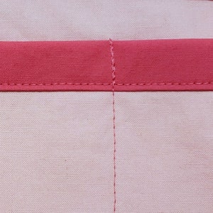 Close-up view of light pink fabric, with darker pink trim and stitching.