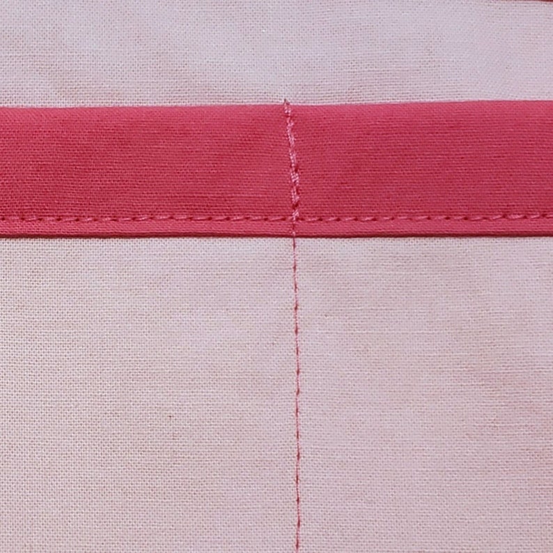 Close-up view of light pink fabric, with darker pink trim and stitching.