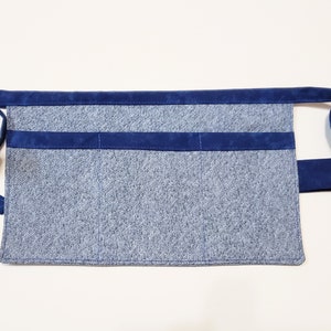 Blue cotton toolbelt for small children, with three large pockets and navy trim and ties. There is an added loop off to one side for hanging a small tool, such as a hammer.