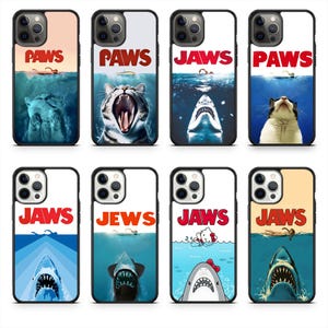 May include: A collection of phone cases with various designs. Some cases feature the word "PAWS" with cat imagery, while others display "JAWS" with shark illustrations. One case has "JEWS" and another has a Hello Kitty shark.