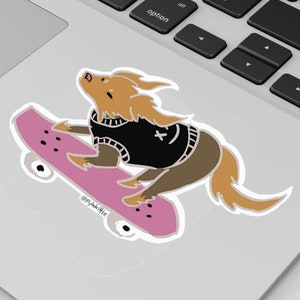 Puede incluir: Una pegatina con un perro de dibujos animados montando en monopatín. El perro es marrón y canela, con un suéter negro con una estrella blanca y una carita sonriente. El monopatín es rosa con ruedas negras. La pegatina está en un portátil.