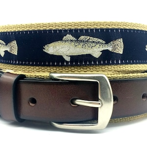 May include: A brown leather belt with a tan canvas strap featuring a repeating pattern of embroidered trout fish on a navy blue background. The belt has a silver buckle.