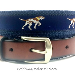 May include: A brown leather belt with a silver buckle. The belt features a navy blue webbing with embroidered dog illustrations. The text "Webbing Color Choices" is visible at the bottom of the image.