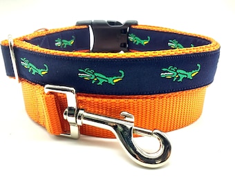 May include: Orange and navy blue dog collar with a repeating alligator pattern. The collar has a silver metal buckle and a silver metal hook.