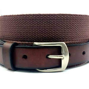 Puede incluir: Un cintur&oacute;n de cuero marr&oacute;n con una correa de lona y una hebilla plateada.