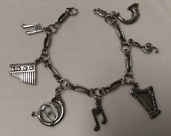 May include: A silver charm bracelet with musical instrument charms, including a harp, a trumpet, a flute, and musical notes.