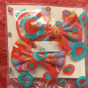 Vintage Avon vinyl rosettformade skoklämmor med ett färgglatt knappmönster i en oöppnad påse