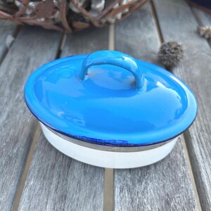 May include: A blue enamel lid with a white rim and a handle. The lid is oval shaped and has a glossy finish.