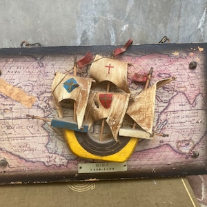 May include: A wooden model of the Nina, one of Christopher Columbus's ships, is mounted on a wooden plaque with a map background. The plaque has a small metal plate with the text "NINA 1492-1506".
